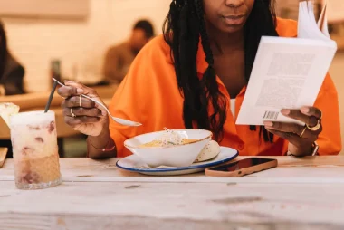 a cropped image of an African-American woman reading a book while eating a dinner