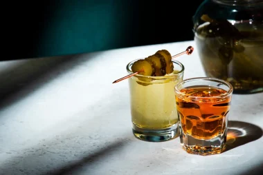 Pickleback, alcoholic cocktail made from cucumber pickle and whiskey in small shot glasses. Hard light and shadows